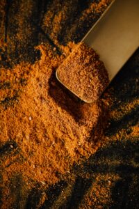 From above of pile of multicolored mix of curcuma and powdered peppers on black surface and wooden spatula